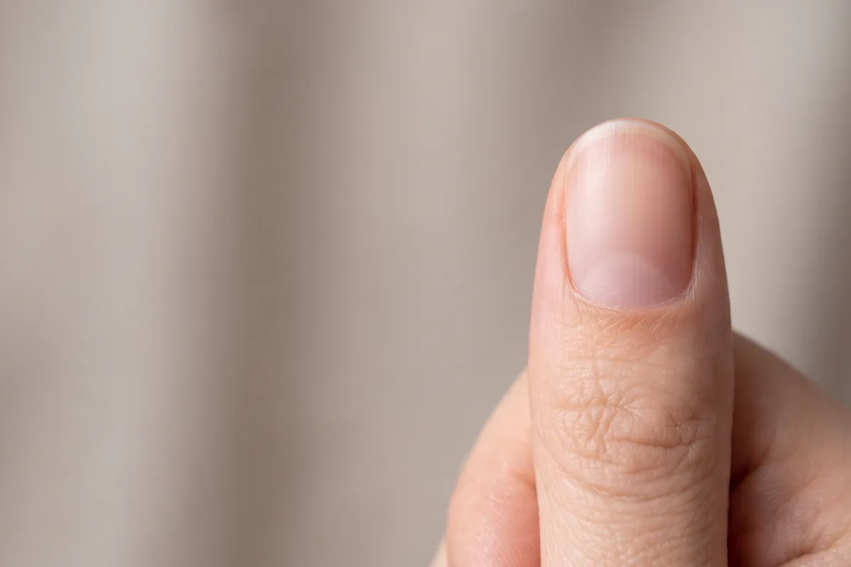 Close-up of a thumb and its thumbnail against light fabric